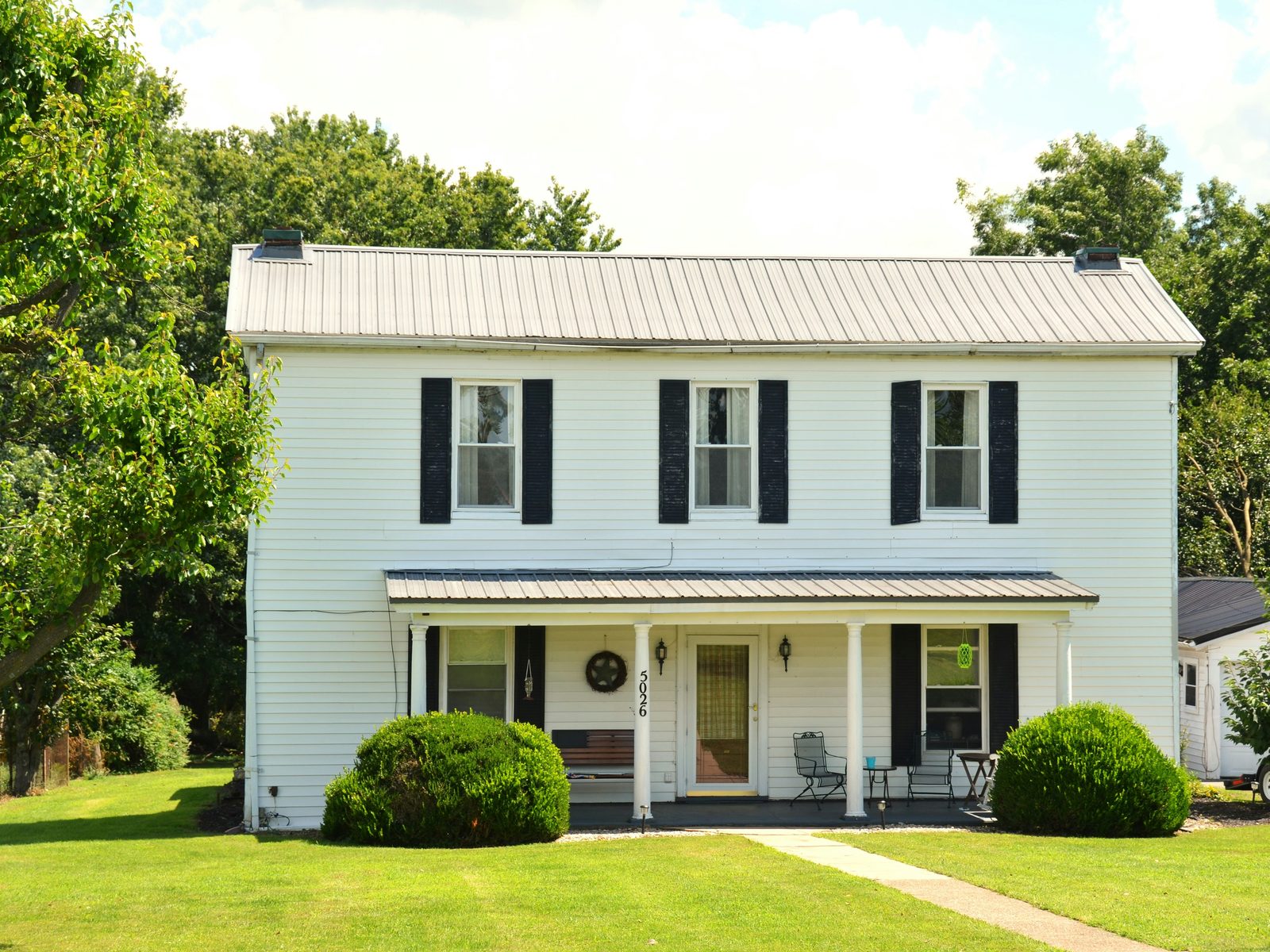 A white clapboard house with black shutters and a covered front porch
