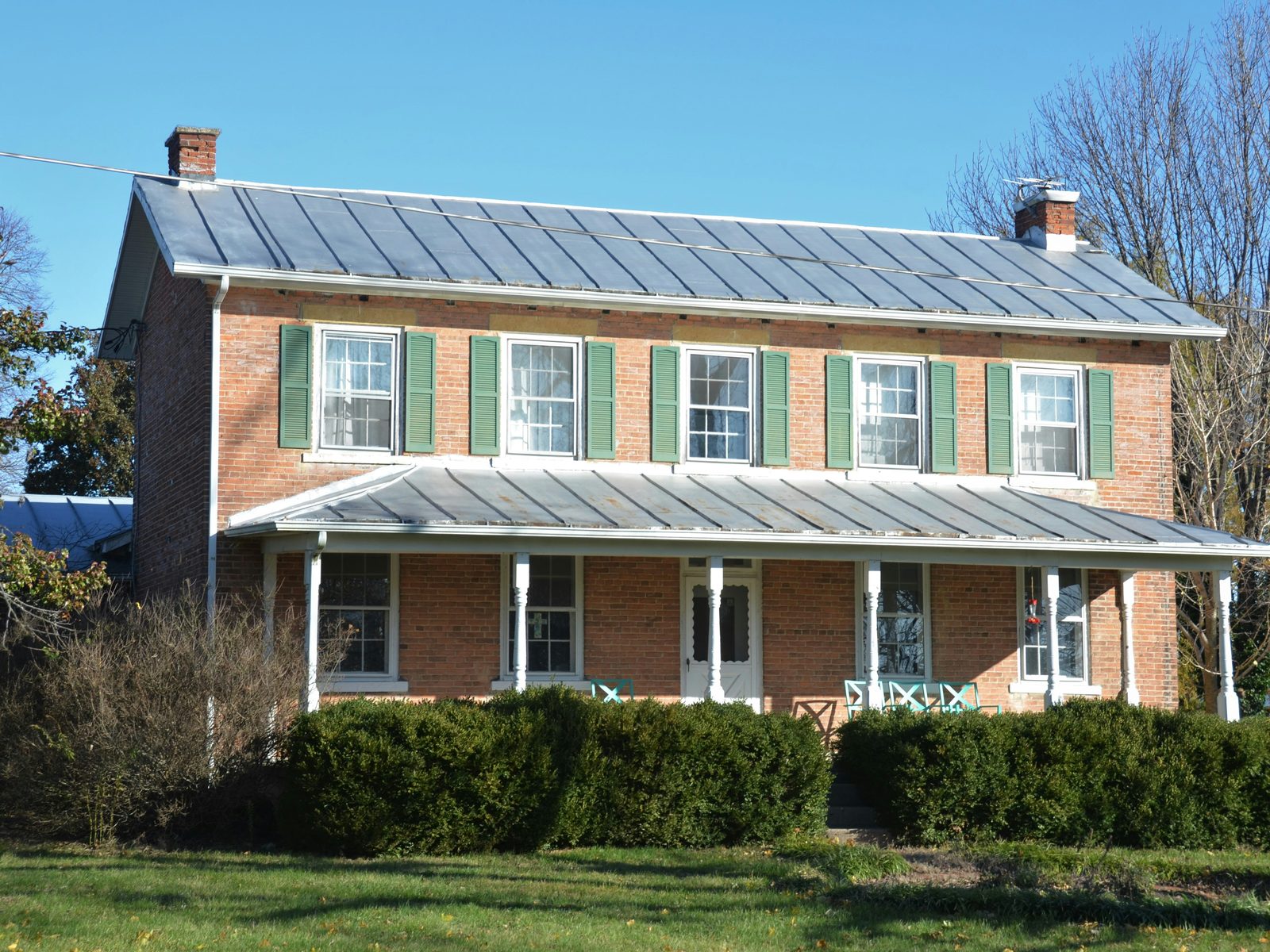 A brick farmhouse with a standing-seam metal roof and a full-width porch