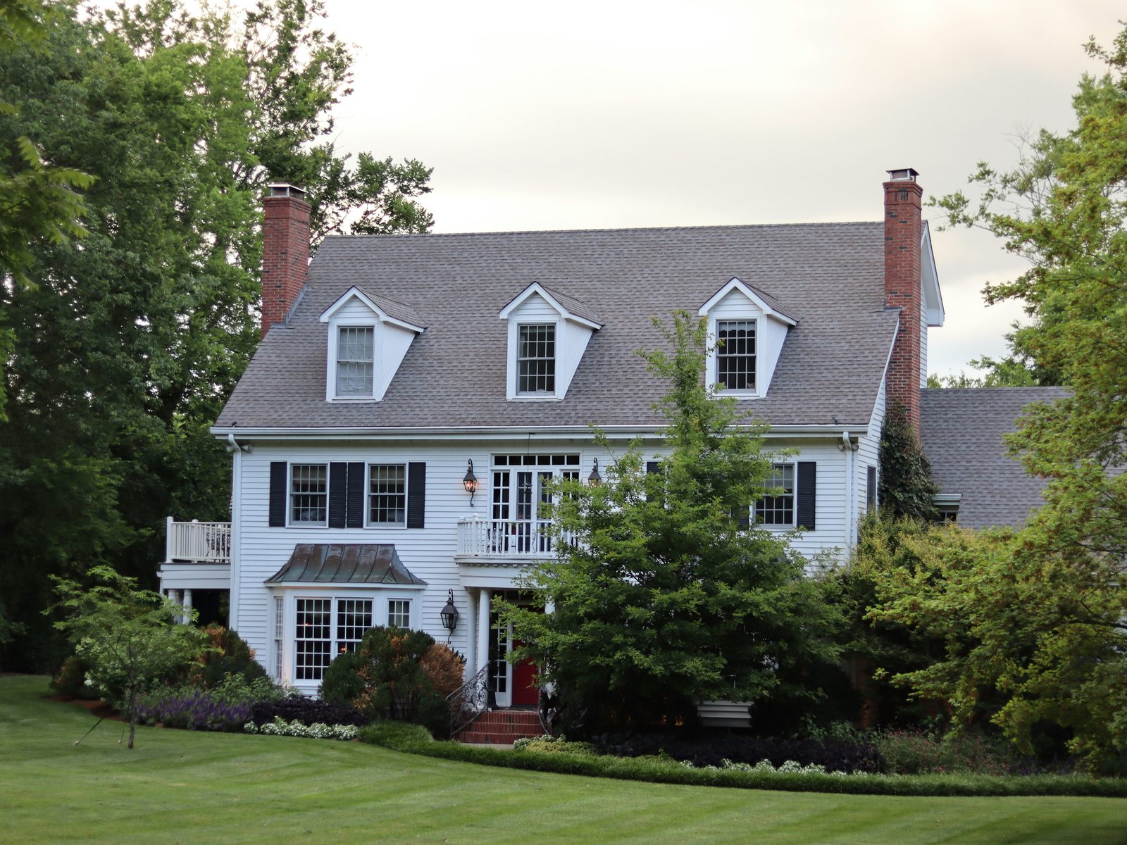 A large white colonial home with dormer windows and a deep front lawn