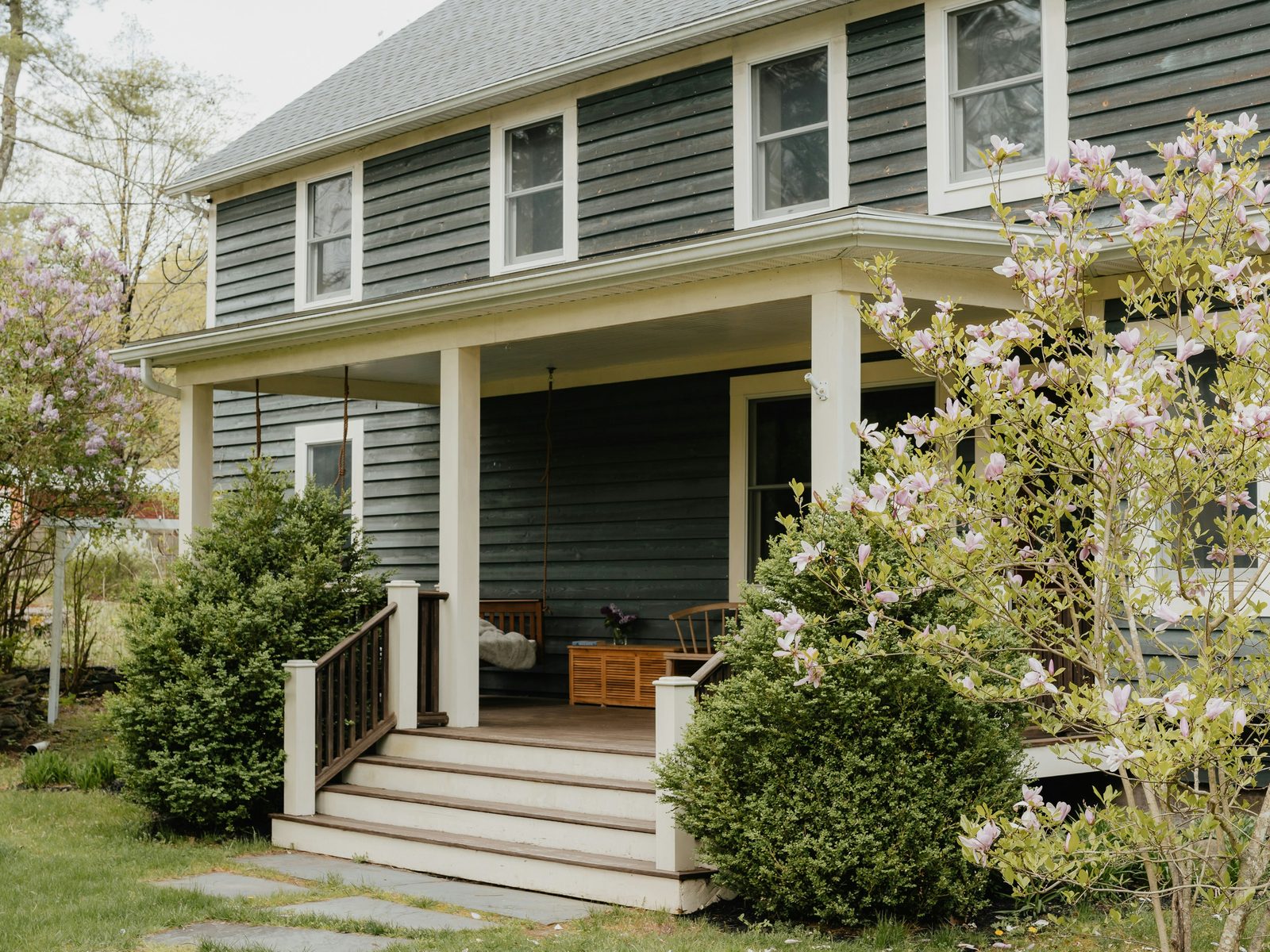 A grey clapboard house with a covered front porch and steps