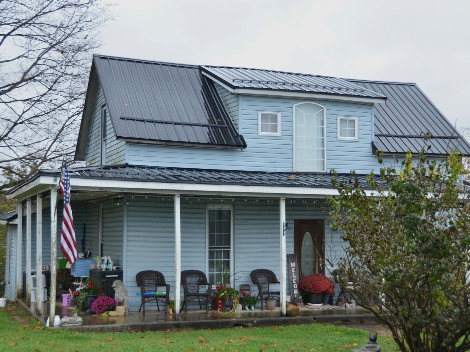 A light blue clapboard house with a wide front porch and an American flag by the door